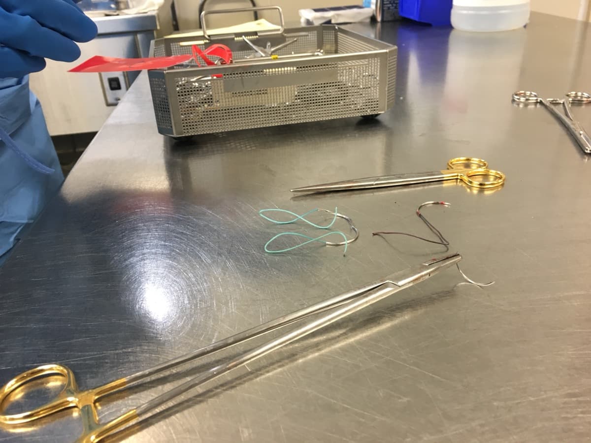 Gloved hands working with surgical instruments and a sterilization basket on a stainless table